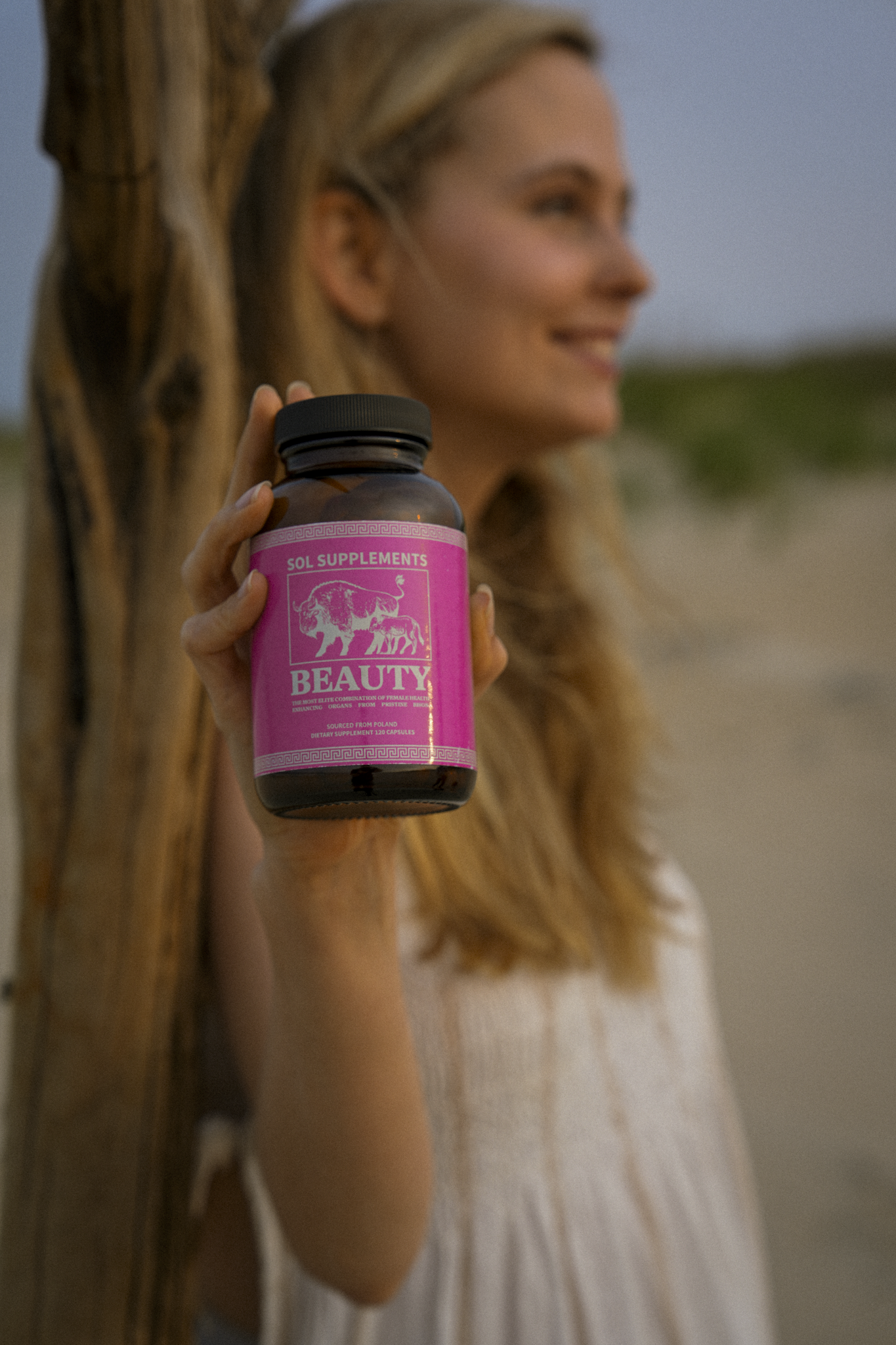 Woman holding a bottle labeled 'Beauty' against a natural background